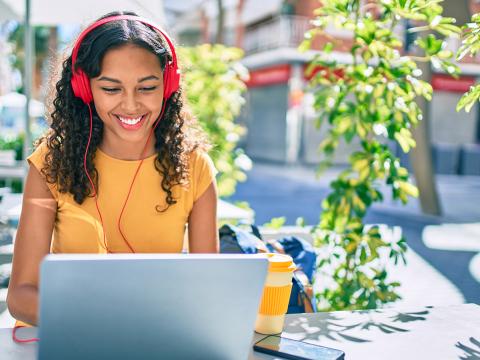 Student with headphones on looking at her laptop and smiling