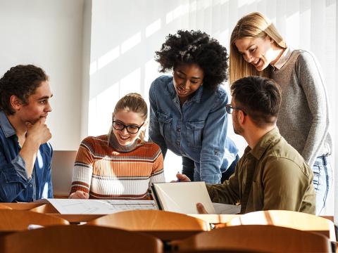 Five students sitting and standing around table.